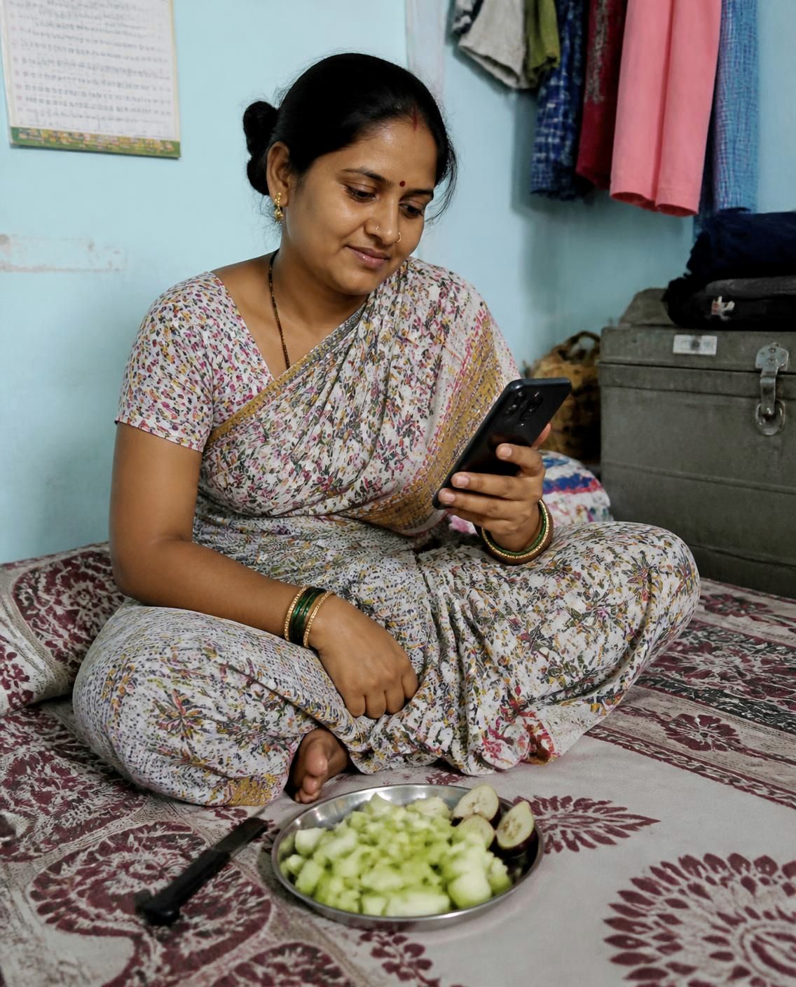 Homemaker in a cotton saree pausing her chores to check a grocery app on her smartphone