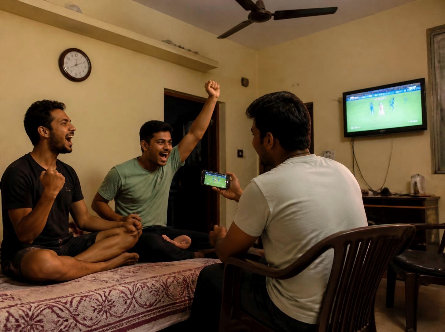 Three young friends cheering a cricket match on a smartphone and TV at home